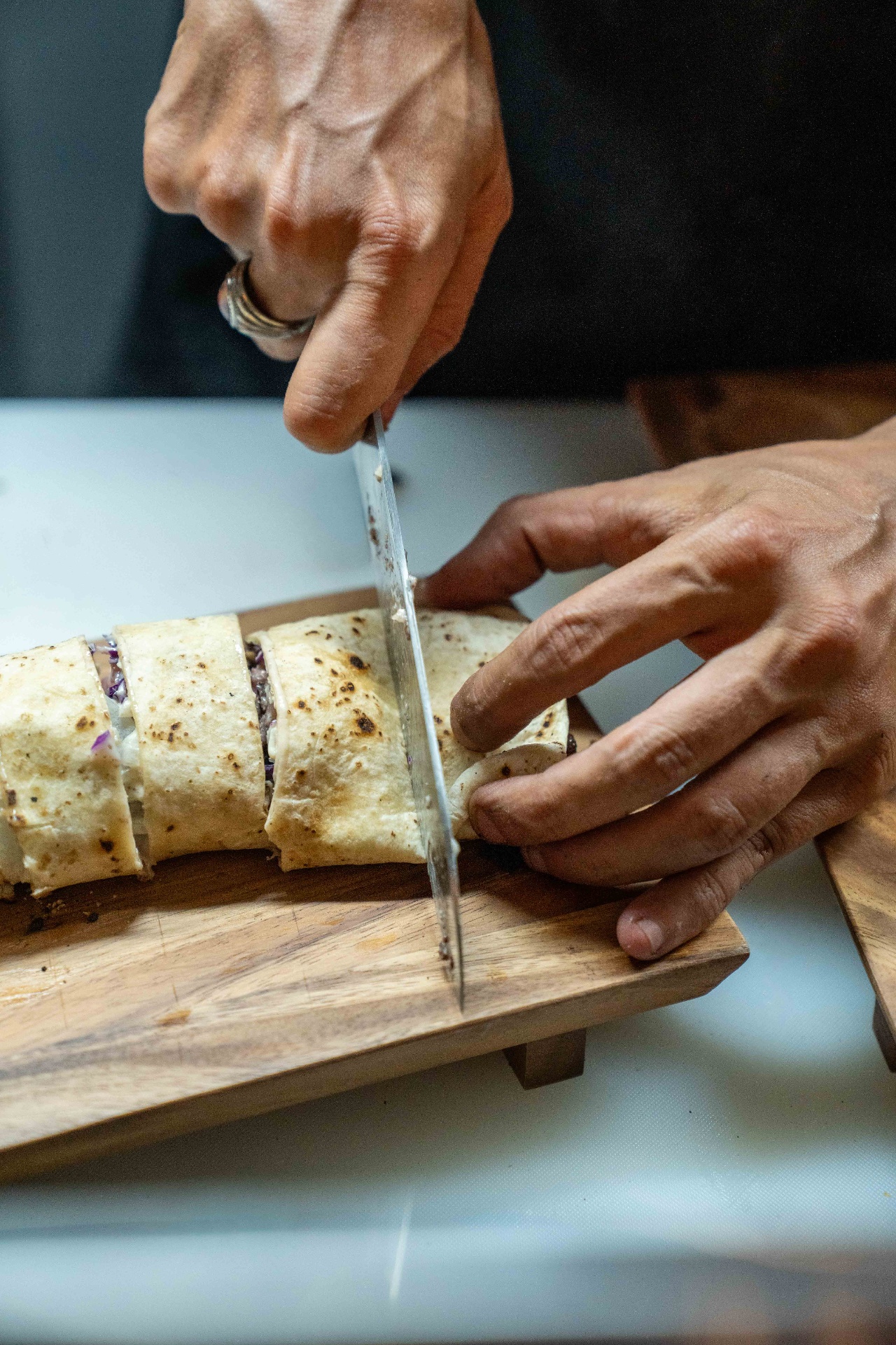 Chef slicing a finished shawarma wrap on a wooden board