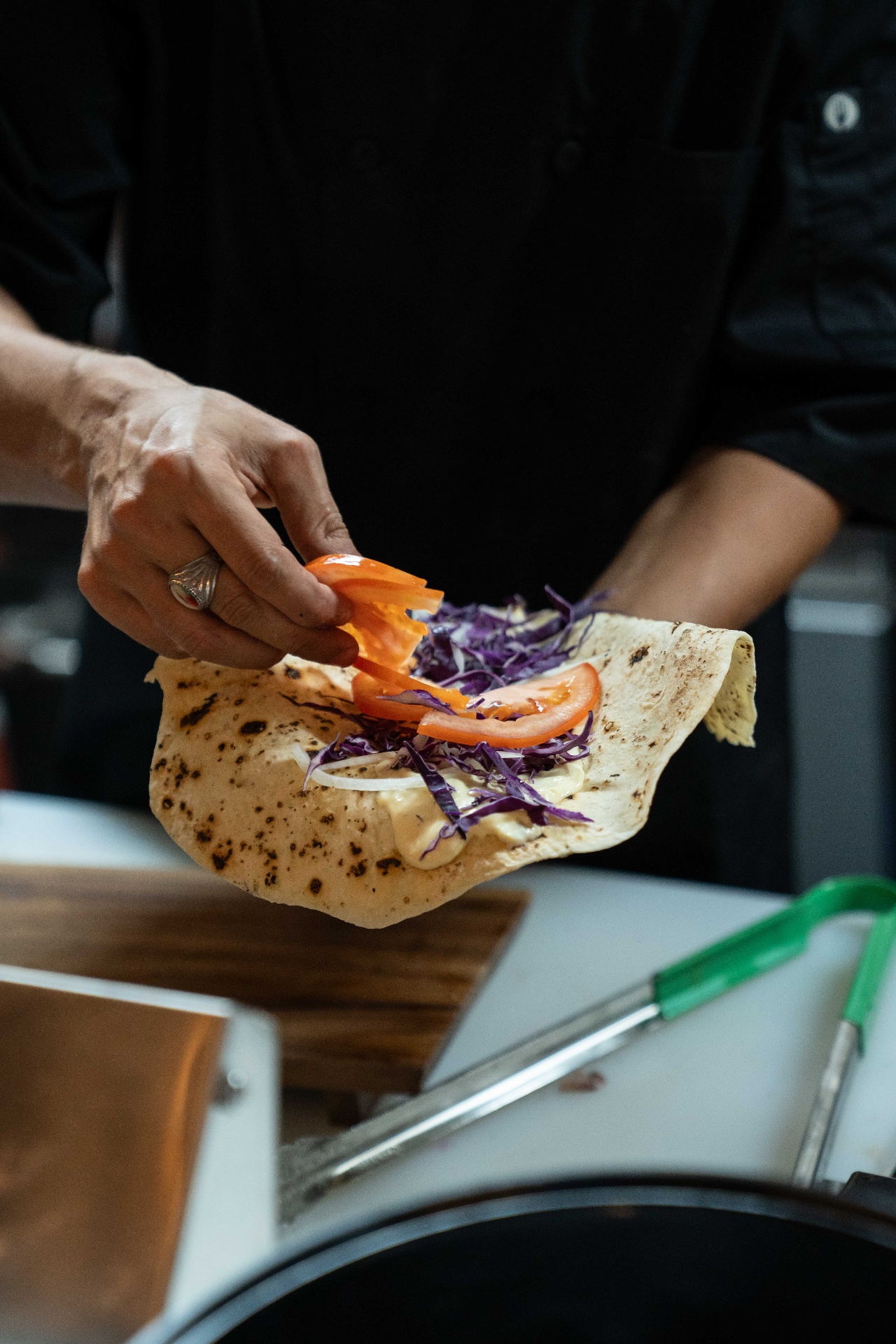 Chef assembling a fresh shawarma wrap with tomato, onion, and red cabbage