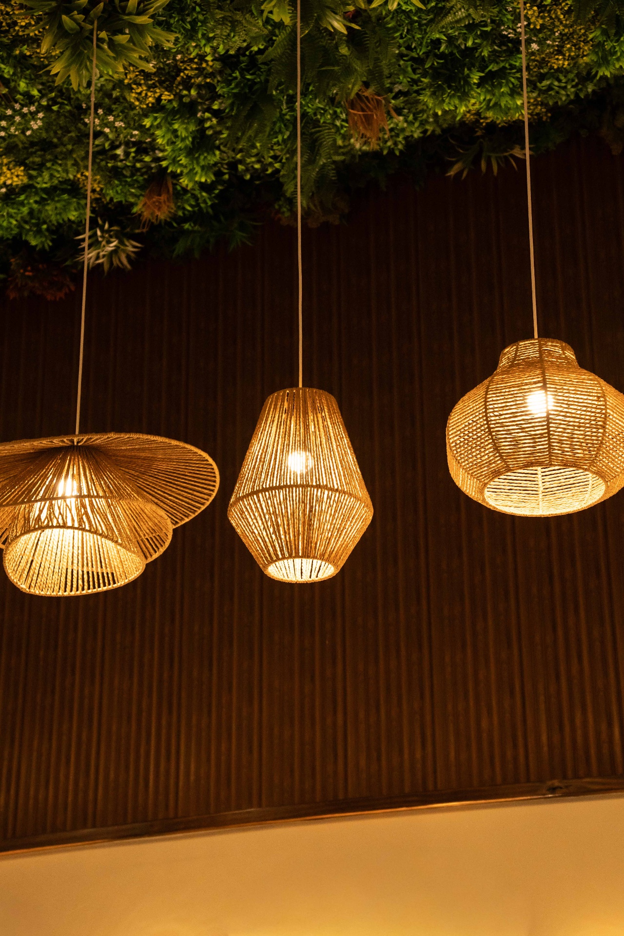 Woven rattan pendant lights glowing against a lush green wall at Yallah