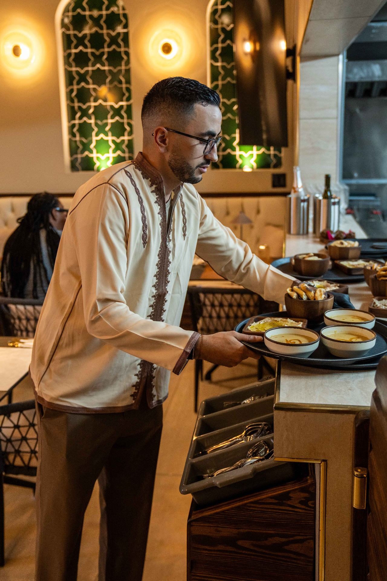 Server in traditional embroidered shirt carrying a tray of mezze